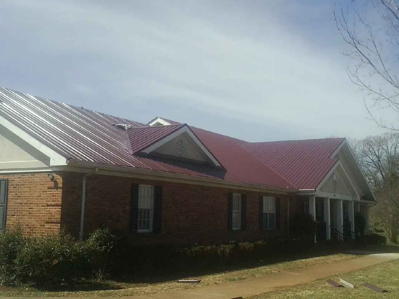 Red metal roof with gabled entries on a long brick building, from a Hail Damage Roof Repair job in Carrabelle