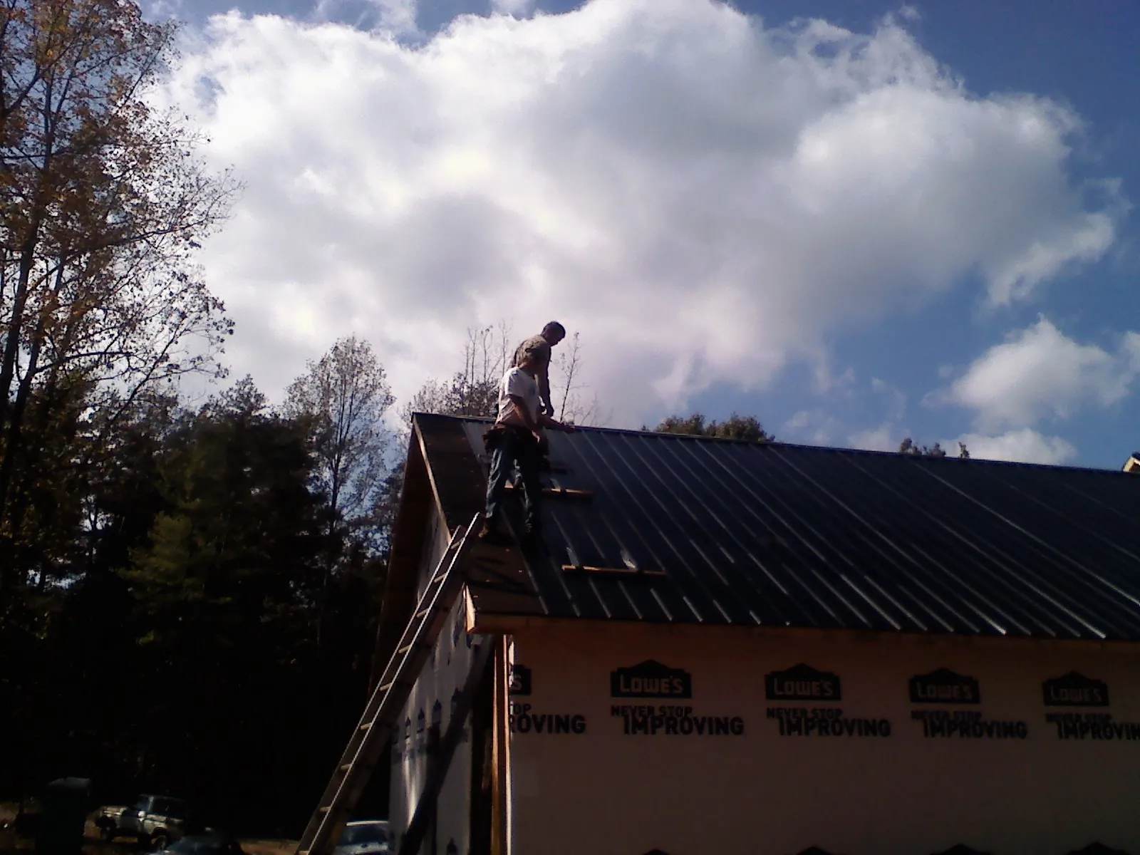 Roofer fastening dark metal panels high against a cloudy sky, from a Roof Inspection job in Carrabelle