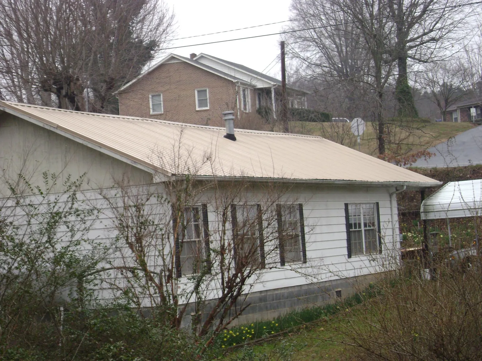Tan metal roof on a white sided house set into a hillside — Commercial Roofing by Roofing Brothers in Carrabelle